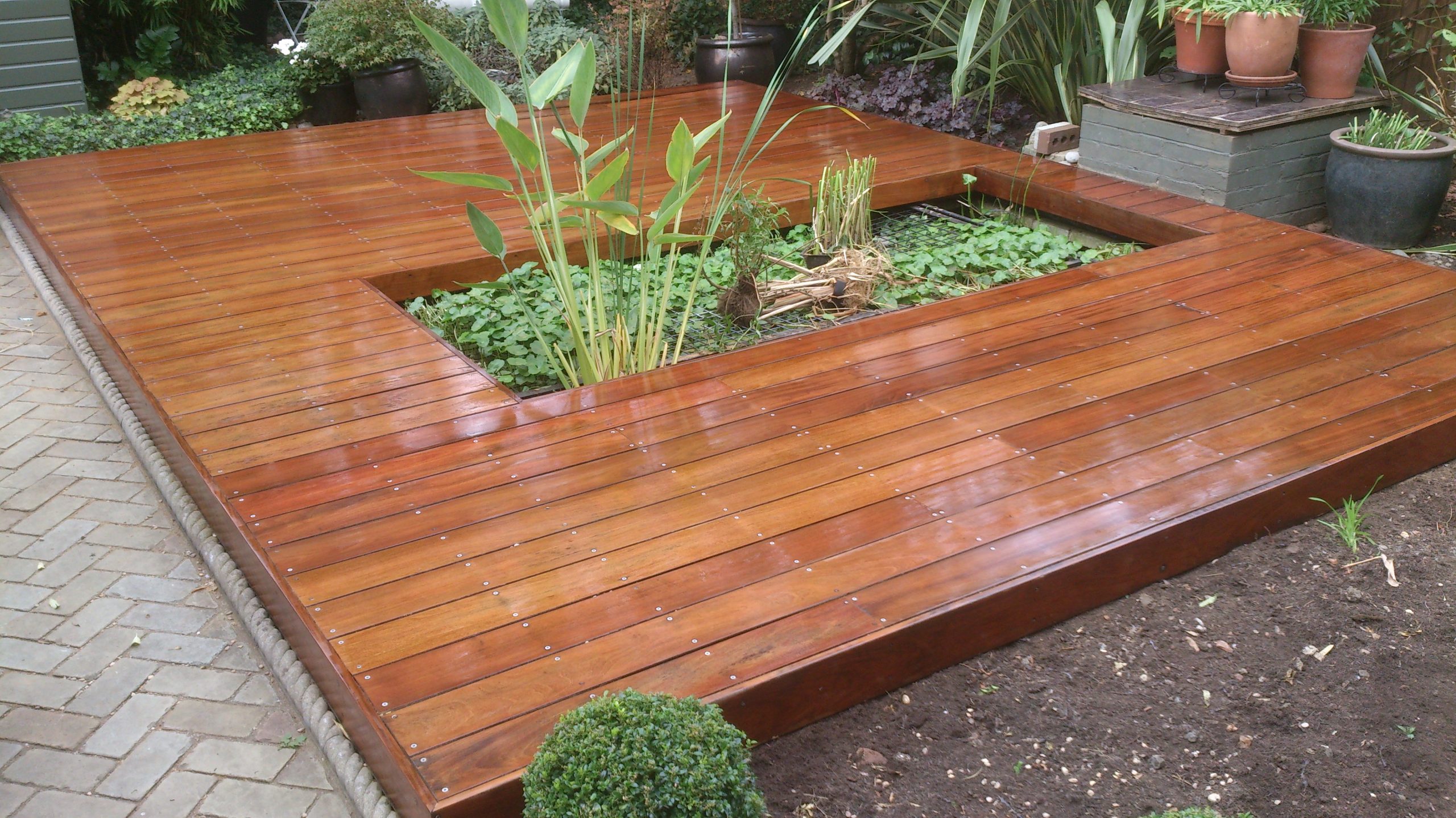 Freshly restored hardwood timber decking after Deck Sanding in Walthamstow, creating a smooth, glossy garden deck floor around a planted feature bed.