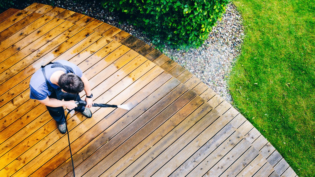 Man cleaning softwood timber decking with a pressure washer in Walthamstow, showing why proper Deck Sanding is safer for the garden deck floor.