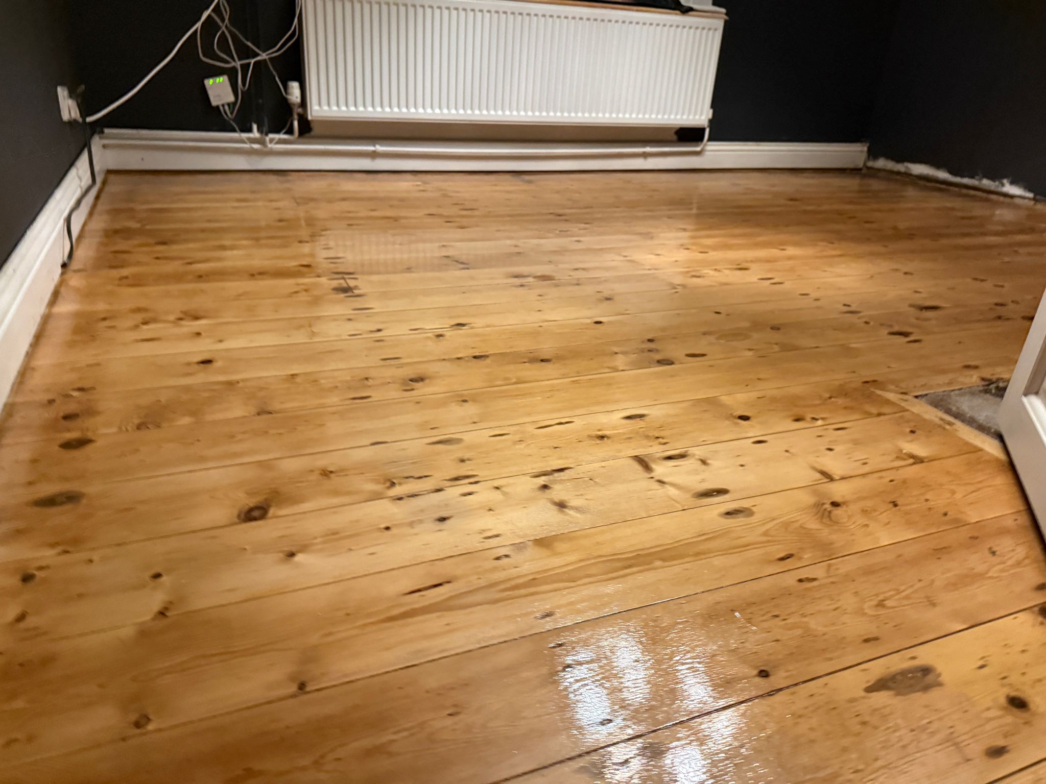 Wood Floor Sanding in Walthamstow on gloss-finished pine softwood floorboards, showing a smooth, freshly restored wooden floor in a dark-walled room.