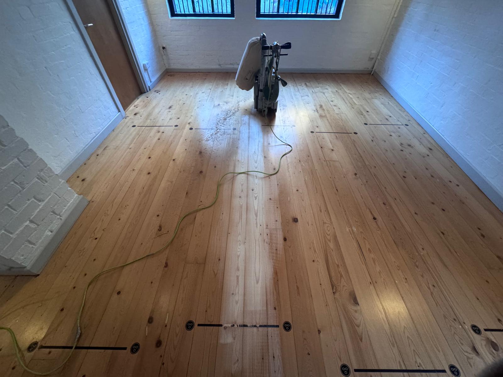 Wood Floor Sanding in Walthamstow on solid pine floorboards, showing a professional sanding machine restoring a bright, smooth finish in a white brick-walled room.