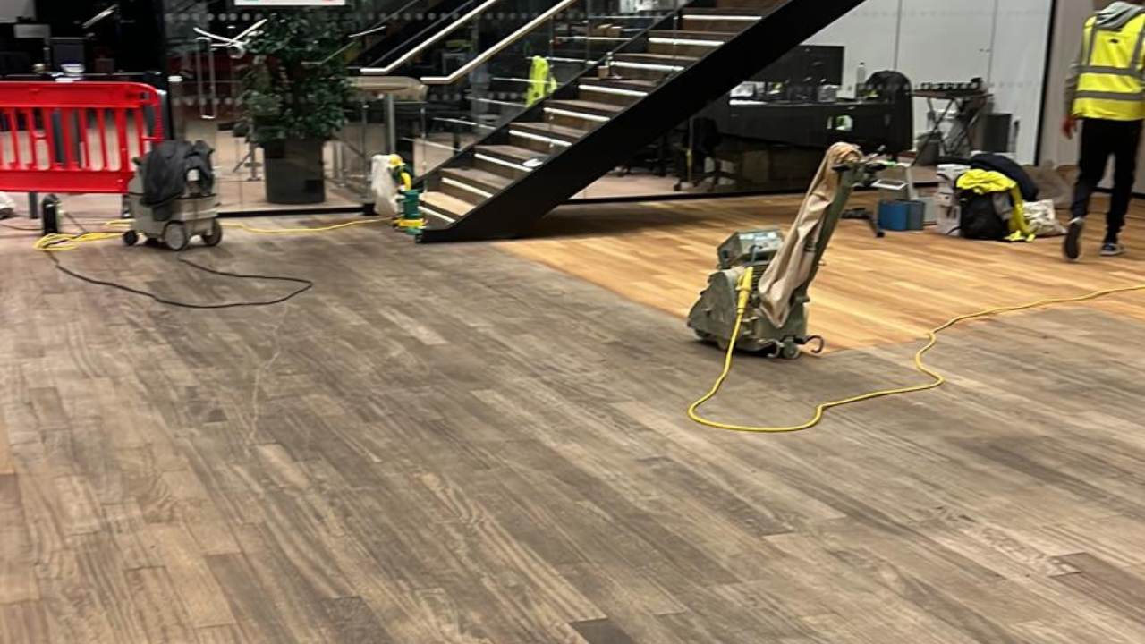 Hardwood Floor Refinishing in Walthamstow showing sanding in progress on an oak plank hardwood floor in a large commercial interior